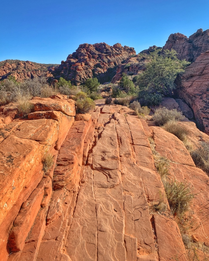 layers of red rock on hiking trail with sage brush and blue skies
